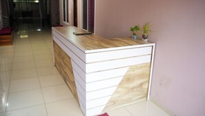 A reception desk with a wooden top and white drawers, a potted plant, and a view of a hallway with a staircase. - GMR Suites (Vythiri)