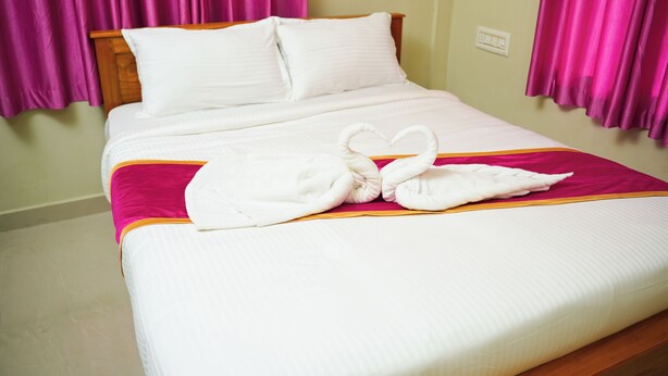 A neatly made bed with white linens, a pink blanket, and a heart-shaped towel arrangement. - GMR Suites (Vythiri)