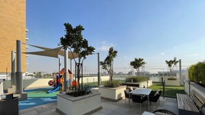 Eine Dachterrasse mit Kinderspielbereich, Außenmöbeln und Blick auf die Stadtlandschaft.
