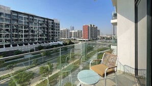 Ein Balkon mit Glasgeländer mit Blick auf eine Stadtlandschaft, mit modernen Gebäuden und einer Straße.