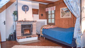 A cozy room with a fireplace, a bed, wooden walls, and a window with curtains.