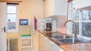 A compact kitchen with a built-in oven, a coffee maker, a sink, and a window with a view of trees.