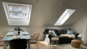 A dining area with a table set for four, a black leather sofa, and a small side table with a lamp. - Apartment 'Schwarzwald-Wellness byHannes' with Mountain View, Wi-Fi and Air Conditioning (Oberkirch)