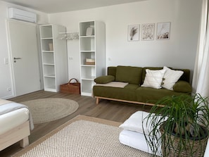 Une pièce avec un canapé vert, des coussins blancs, un panier en osier et une plante en pot.