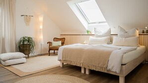 A bedroom with a sloped ceiling, a skylight, a bed with multiple pillows, a chair, a floor lamp, and a potted plant. - Apartment 'Schwarzwald-Wellness byHannes' with Mountain View, Wi-Fi and Air Conditioning (Oberkirch)