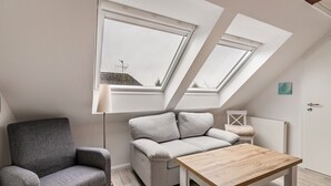 A loft bedroom with a skylight, a grey sofa, a wooden table, and a radiator.