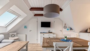 A modern loft bedroom with a skylight, a wooden dining table, white furniture, and a mounted TV.