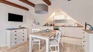 A modern kitchen with white cabinetry, a wooden dining table, and a TV mounted on the wall.