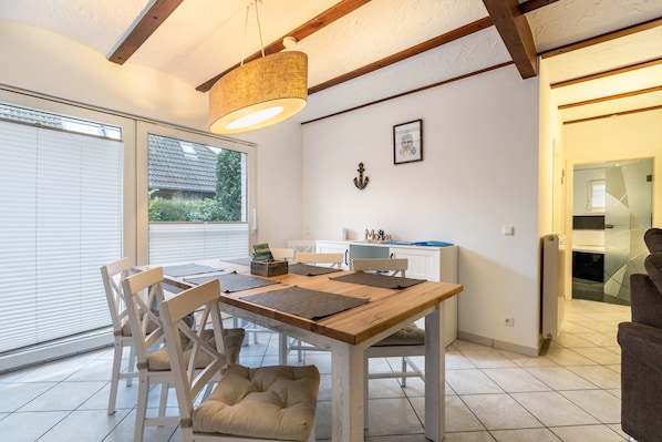 Un espace repas avec une table en bois, des chaises blanches et un luminaire suspendu.