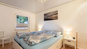 Un dormitorio con cama, mesitas de noche, una ventana y una obra de arte colgada en la pared.