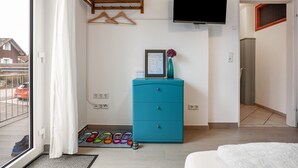 Een kamer met een blauwe ladekast, een aan de muur bevestigde televisie, een deur naar een andere kamer en uitzicht buiten door een raam.