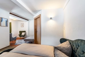Un dormitorio con cama, un sillón verde, una puerta de madera y una lámpara fijada a la pared.