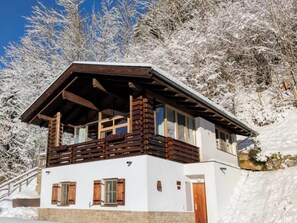 A wooden chalet with a balcony, white walls, and a wooden door.