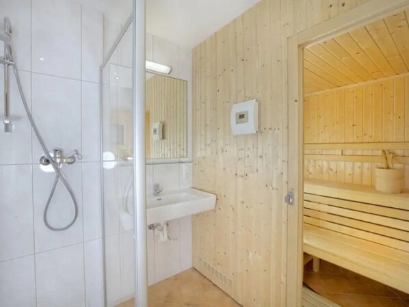 A modern bathroom with a glass shower enclosure, a sink, and a wooden sauna area.