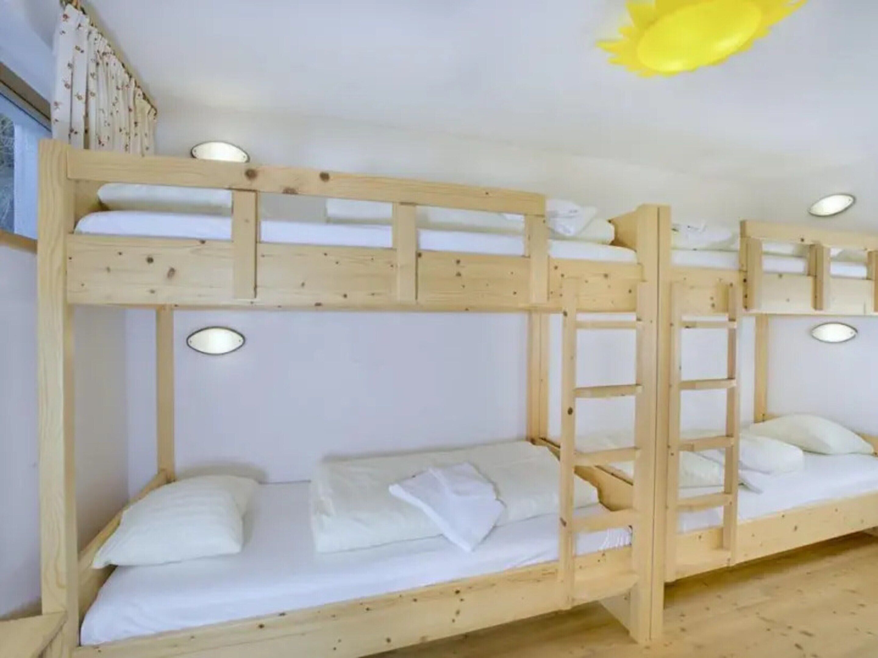 A bunk bed with a ladder, white bedding, and a ceiling light fixture.