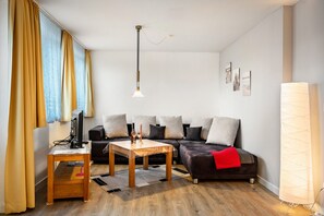 Moderni olohuone, jossa on sohva, sohvapöytä, televisio ja lamppu.