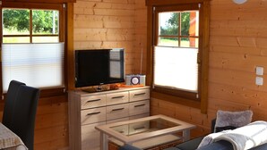 L’intérieur d’un chalet en bois, avec un canapé, un téléviseur, une radio et une fenêtre.