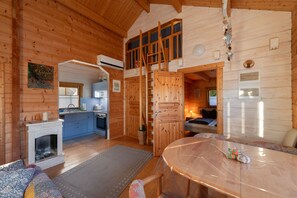 A wooden cabin interior with a kitchen, dining area, and a loft bedroom.
