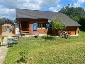 Puuinen mökki, jossa on terassi, polkupyörä ja satelliittiantenni.