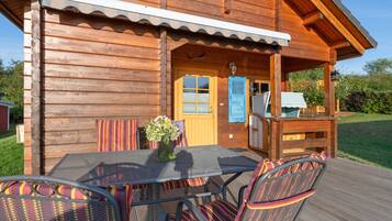 Puinen mökki, jossa on terassi, jonka yhteydessä on pöytä ja tuolit, maljakko kukkia varten sekä pieni ulkokeittiö.