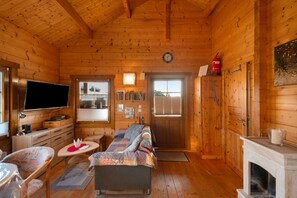 A cozy cabin interior with a sofa, a flat-screen TV, a fireplace, and wooden walls.