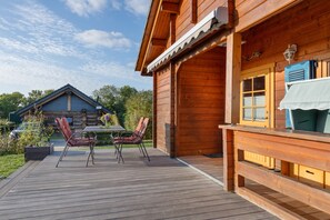 A wooden cabin with a deck, two chairs, and a table.