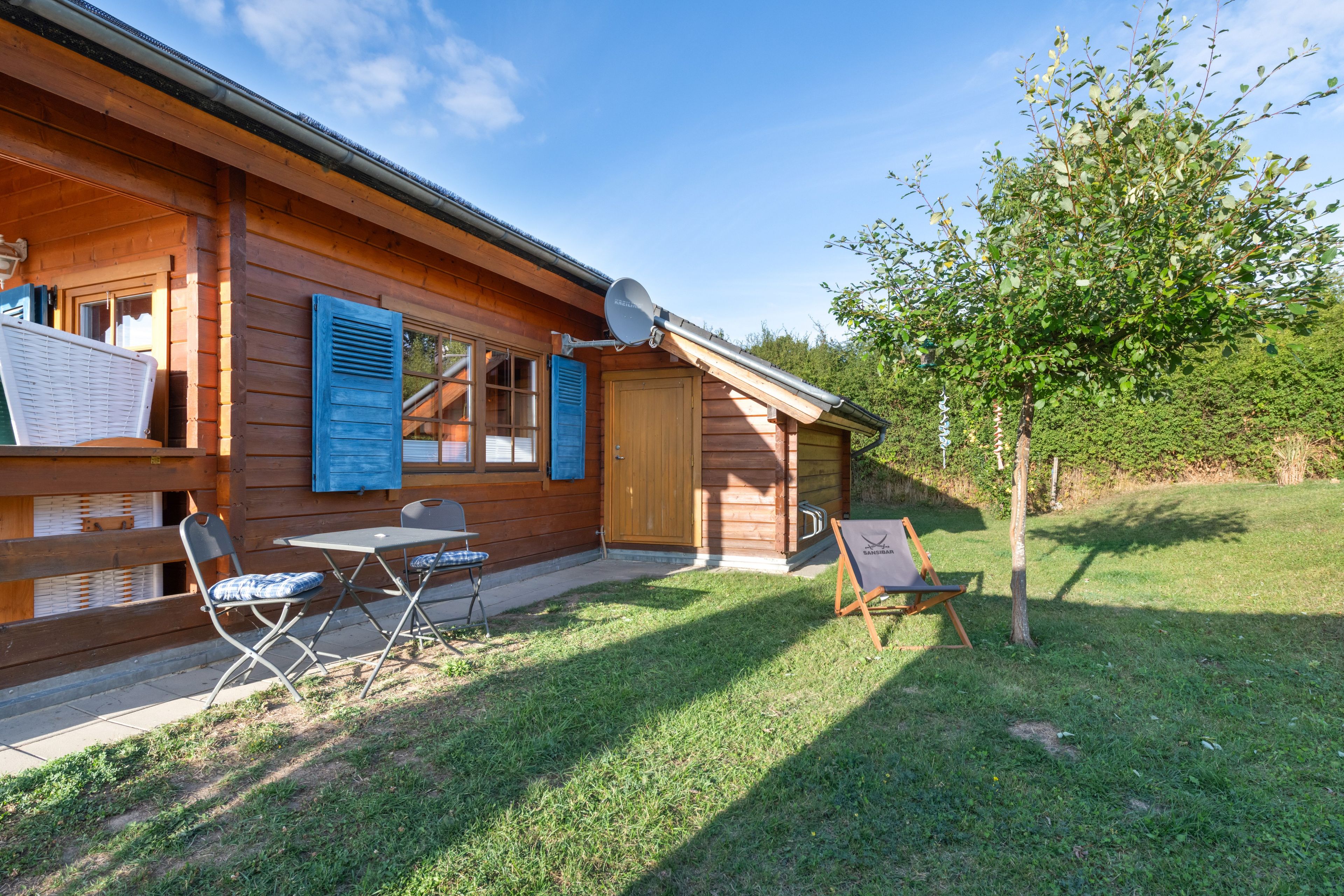 Eine Holzhütte mit einer Terrasse, einem Tisch mit Stühlen und einem kleinen Baum.