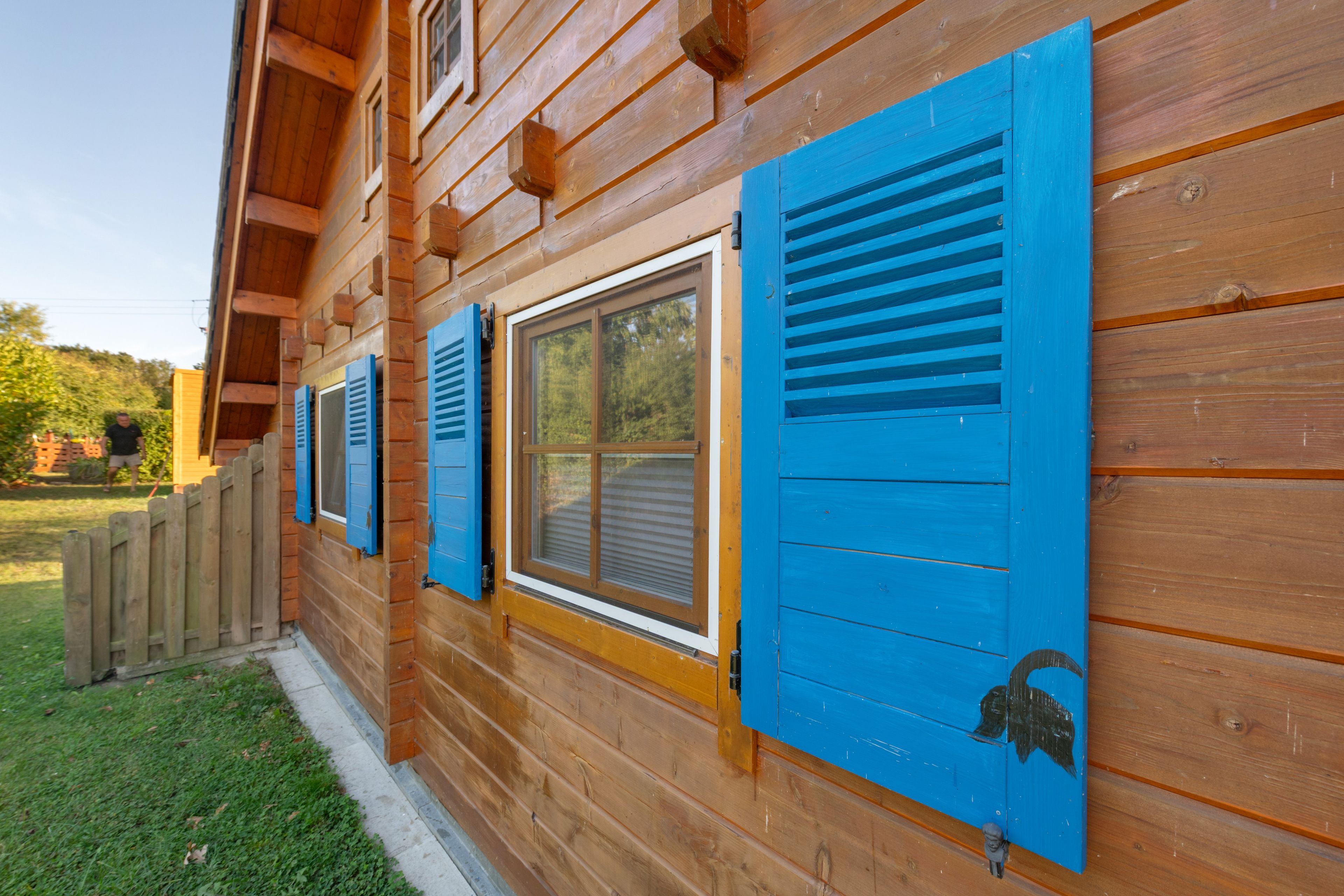 Eine Holzhütte mit blauen Fensterläden und einer kleinen Figur daran.