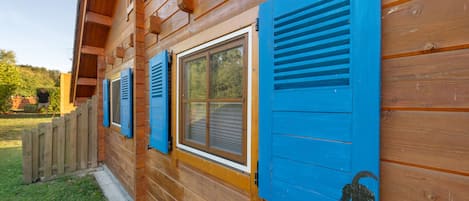 A wooden cabin with blue shutters on the windows and a small figurine attached to the shutter.