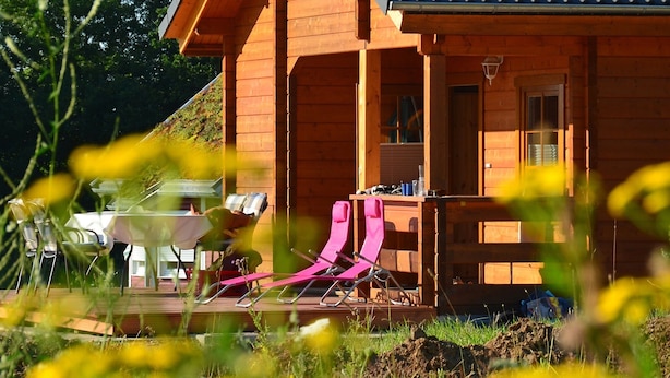 Une cabane en bois avec un toit en pente, une véranda avec des chaises et une table.