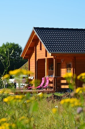 Une cabane en bois avec un toit en pente, une véranda avec des chaises et une table.