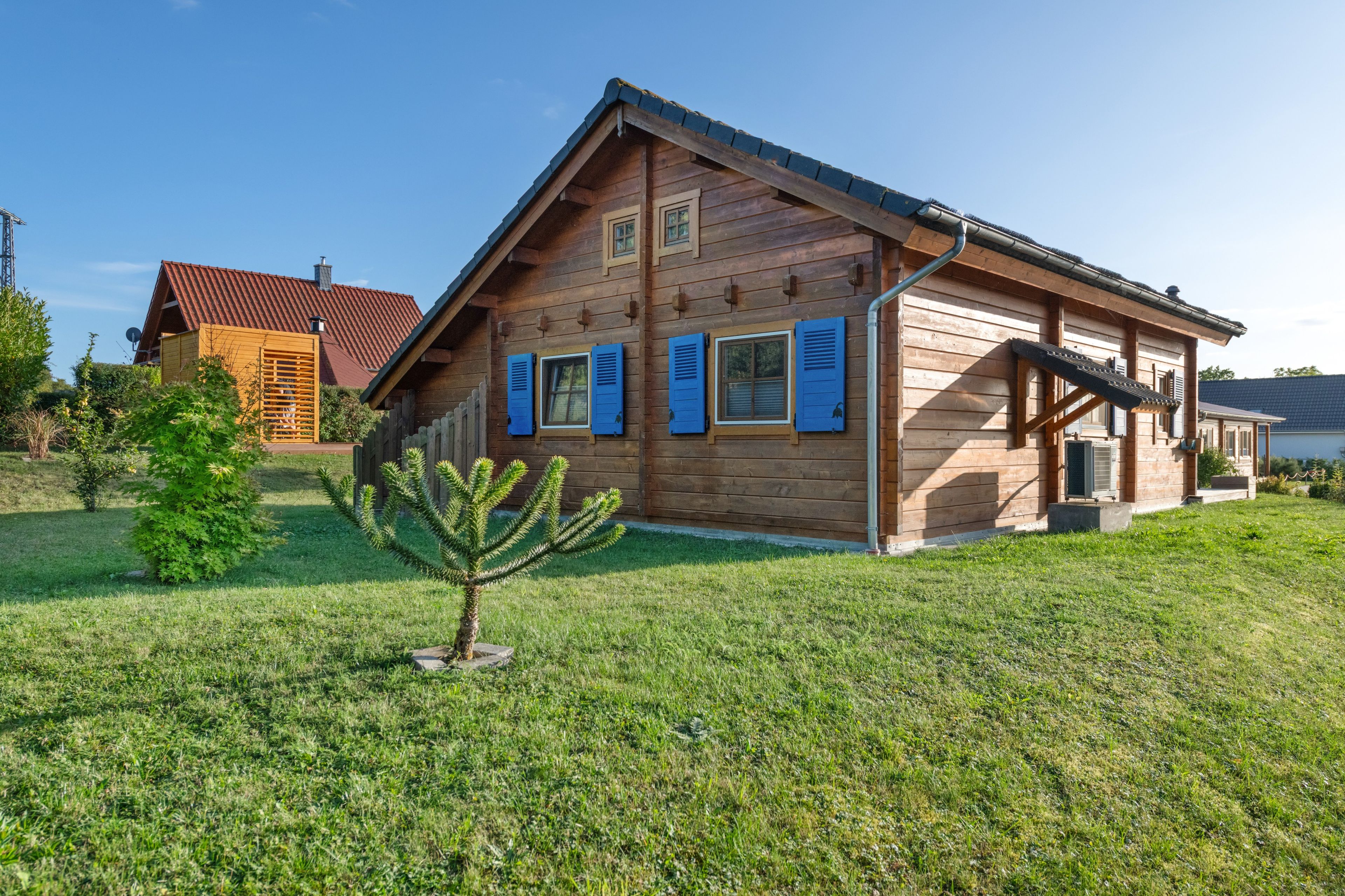 Ein Holzhaus mit geneigtem Dach, ein kleiner Baum im Vorgarten und eine Satellitenschüssel auf dem Dach.
