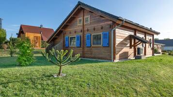 Ein Holzhaus mit geneigtem Dach, ein kleiner Baum im Vorgarten und eine Satellitenschüssel auf dem Dach.