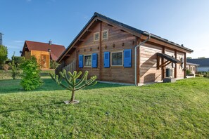 Una casa di legno con tetto spiovente, un piccolo albero nel giardino e un'antenna parabolica sul tetto.