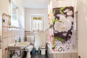 A bathroom with a toilet, sink, and shower curtain with floral design. - Apartment 'Möblierte Wohnung Ferienwohnung' with Shared Terrace, Shared Garden and Wi-Fi (Aicha vorm Wald)