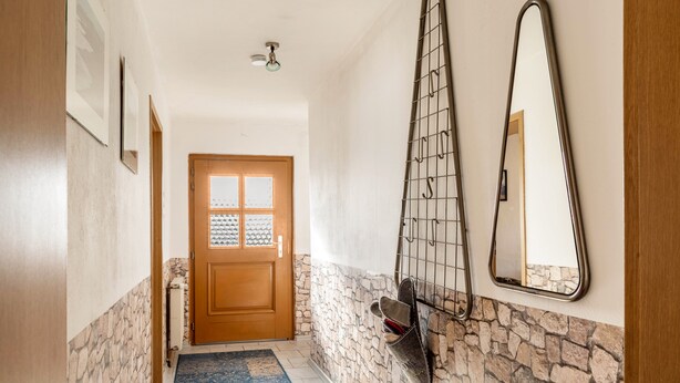 Un pasillo con puerta de madera, pared de piedra, alfombra azul y perchero con zapatos.