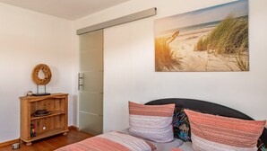 Un dormitorio con una cama, un estante de madera, un cuadro de una playa y una puerta corredera.