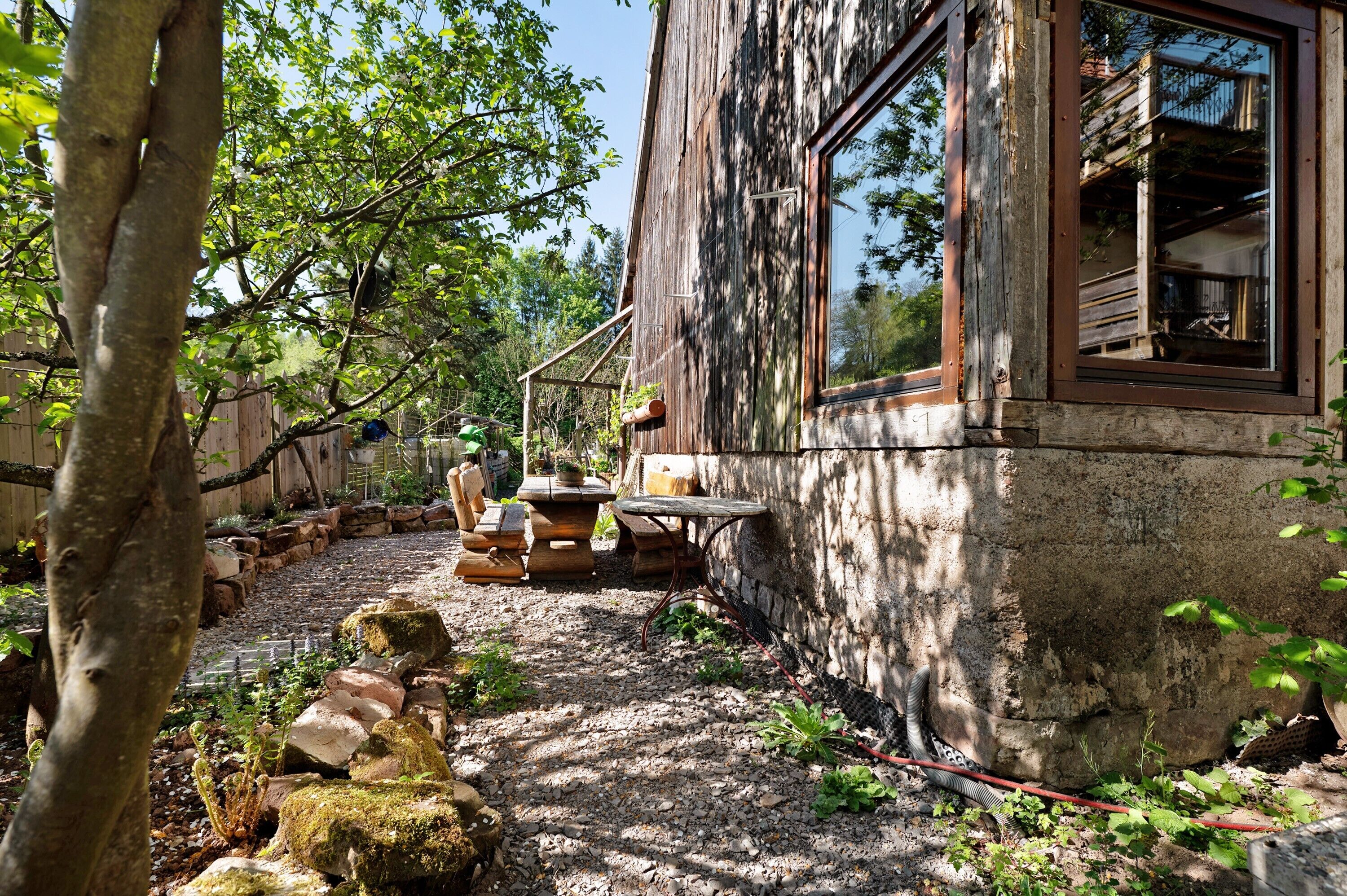 Un bâtiment rustique en bois, doté d’un chemin en pierre, d’un espace extérieur aménagé pour s’asseoir et d’une grande fenêtre.