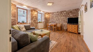 A cozy living room with a stone wall, wooden ceiling, a sofa, a table, a TV, and a fireplace.