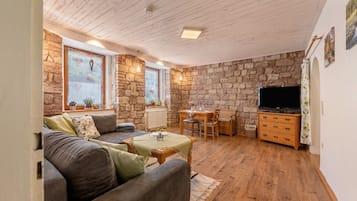 Een gezellige woonkamer met een stenen muur, houten plafond, een bank, een tafel, een televisie en een open haard.
