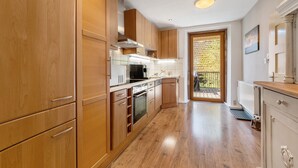A modern kitchen with wooden cabinets, stainless steel appliances, and a view to the outside.