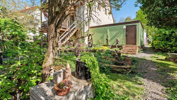 A garden with a tree, a small shed, and a building with a staircase.