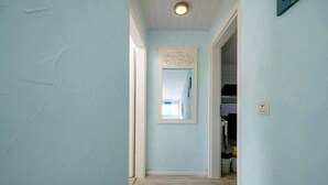 Un passadís amb parets de blau clar, un paviment de fusta i una porta que condueix a una altra habitació.