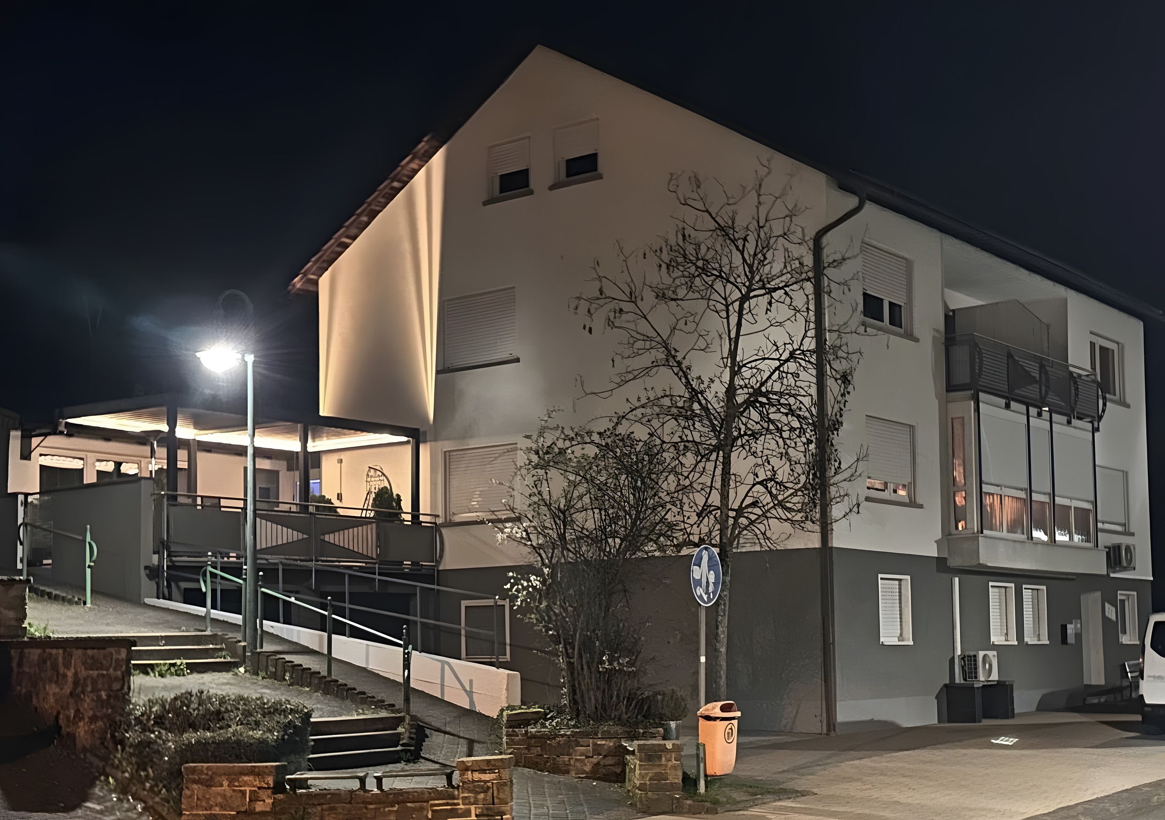 Een gebouw met een trap naar een overdekte ingang, een prullenbak en een lantaarnpaal.