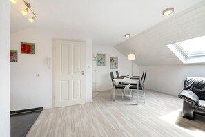 A modern room with a skylight, a dining area with chairs and a table, a black leather sofa, and artwork on the walls.