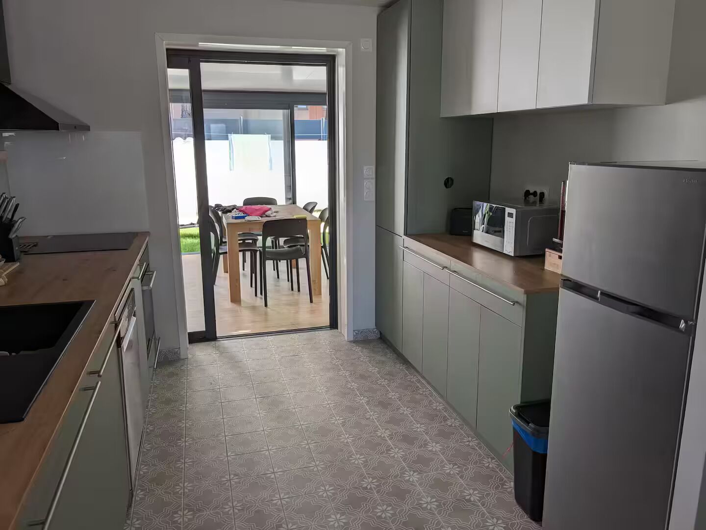 Une cuisine moderne avec un coin repas visible à travers une porte vitrée, comprenant un four à micro-ondes, un réfrigérateur et une table à manger avec des chaises.