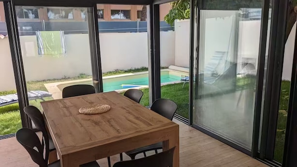 A modern dining area with a wooden table and chairs, large glass doors leading to a pool and garden. - Petite Bulle, a place of calm and relaxation close to the town center. (Narbonne)