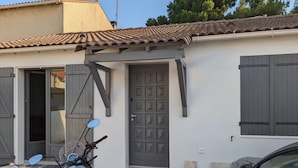 A motorcycle parked in front of a building with a tiled roof, a door with a window, and a car parked nearby. - Petite Bulle, a place of calm and relaxation close to the town center. (Narbonne)