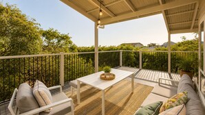 Een overdekt terras buiten, met een tafel en zitplaatsen, omringd door groen.