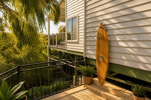 Una tabla de surf de madera montada en la fachada de una casa, un balcón con barandilla y follaje circundante.